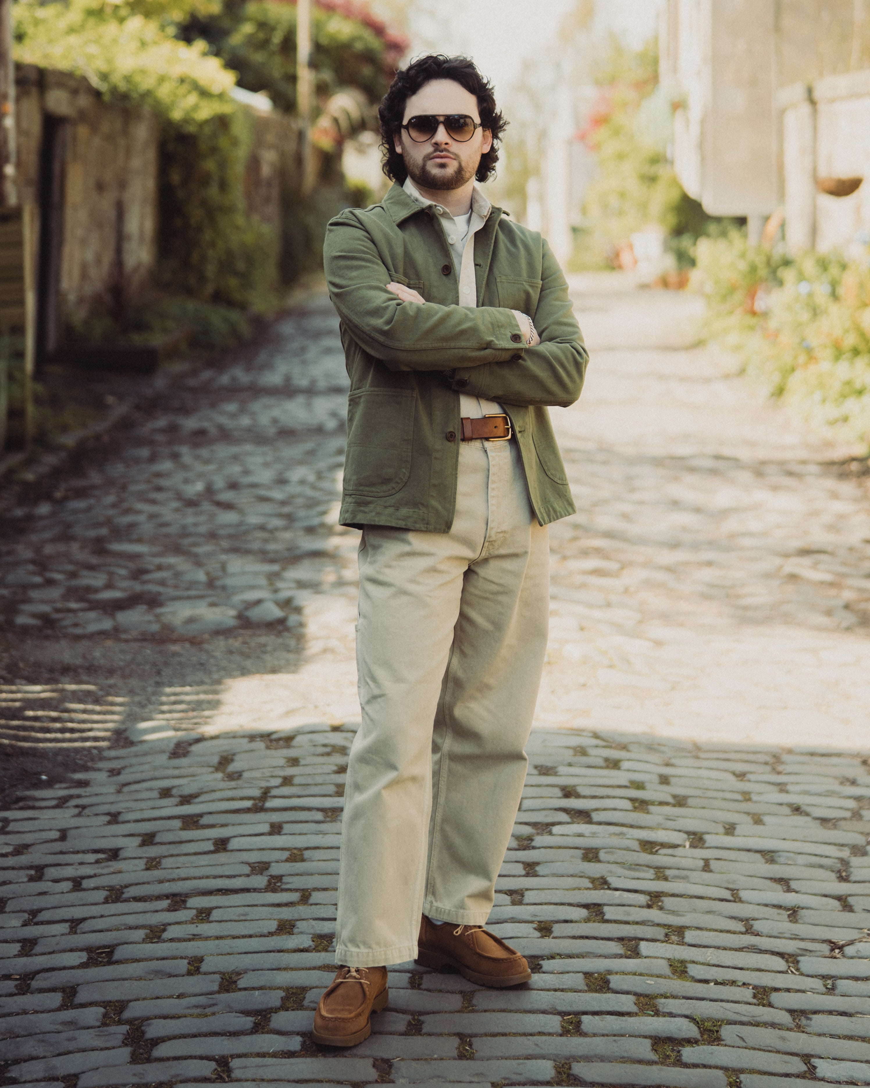 Man standing on a cobblestone street wearing a green jacket and sunglasses.