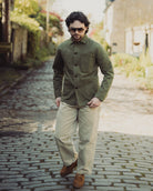 Man wearing a green jacket and beige pants walking on a cobblestone street.