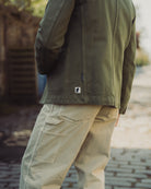 Person wearing a green jacket and beige pants on a blurred outdoor background