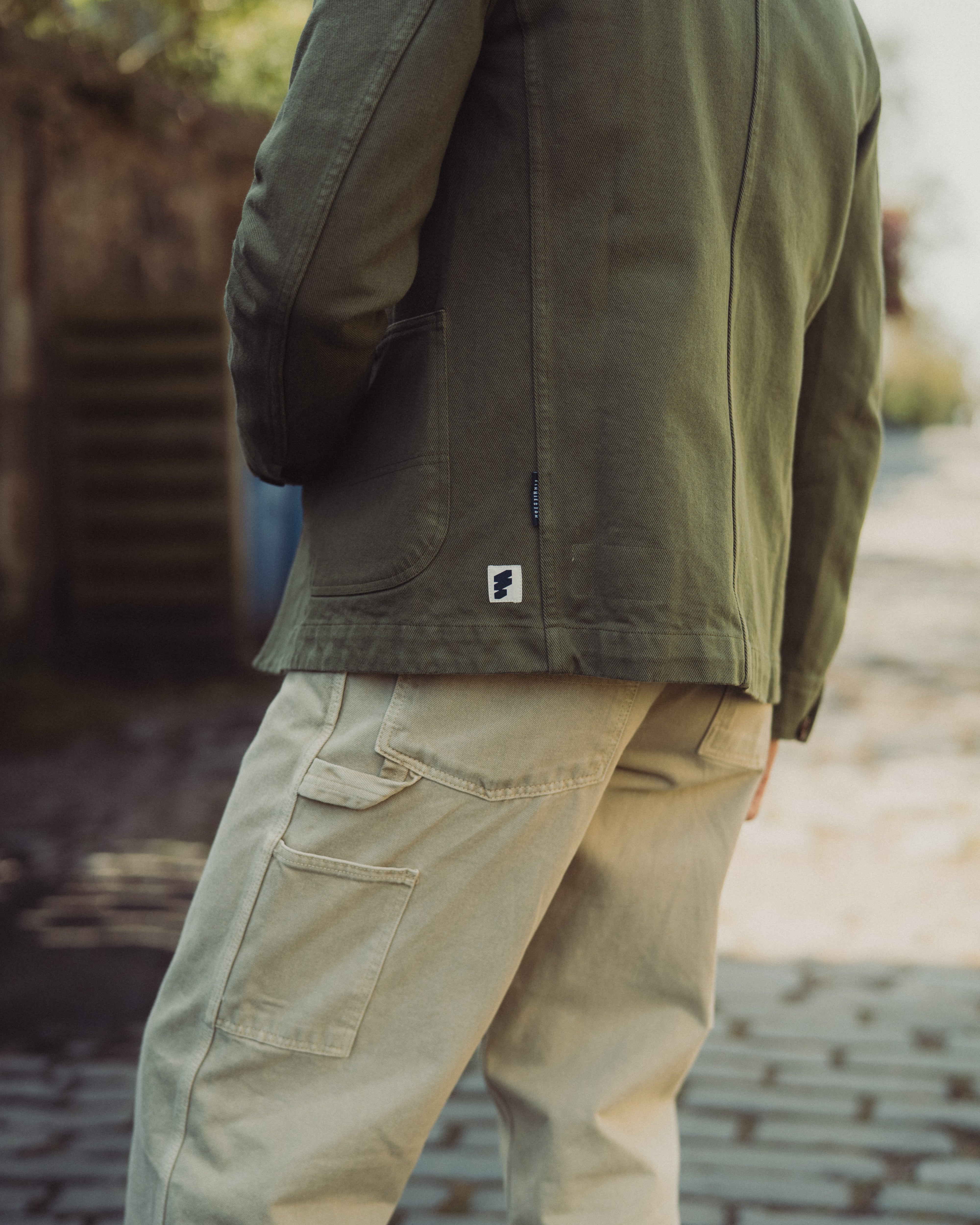 Person wearing a green jacket and beige pants on a blurred outdoor background