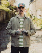 Man wearing a cap and jacket standing on a stone path with greenery