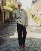 Man standing on a cobblestone path wearing a cap, jacket, and striped shirt.