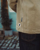 Close-up of a person wearing a beige jacket with a brand logo, blurred indoor background