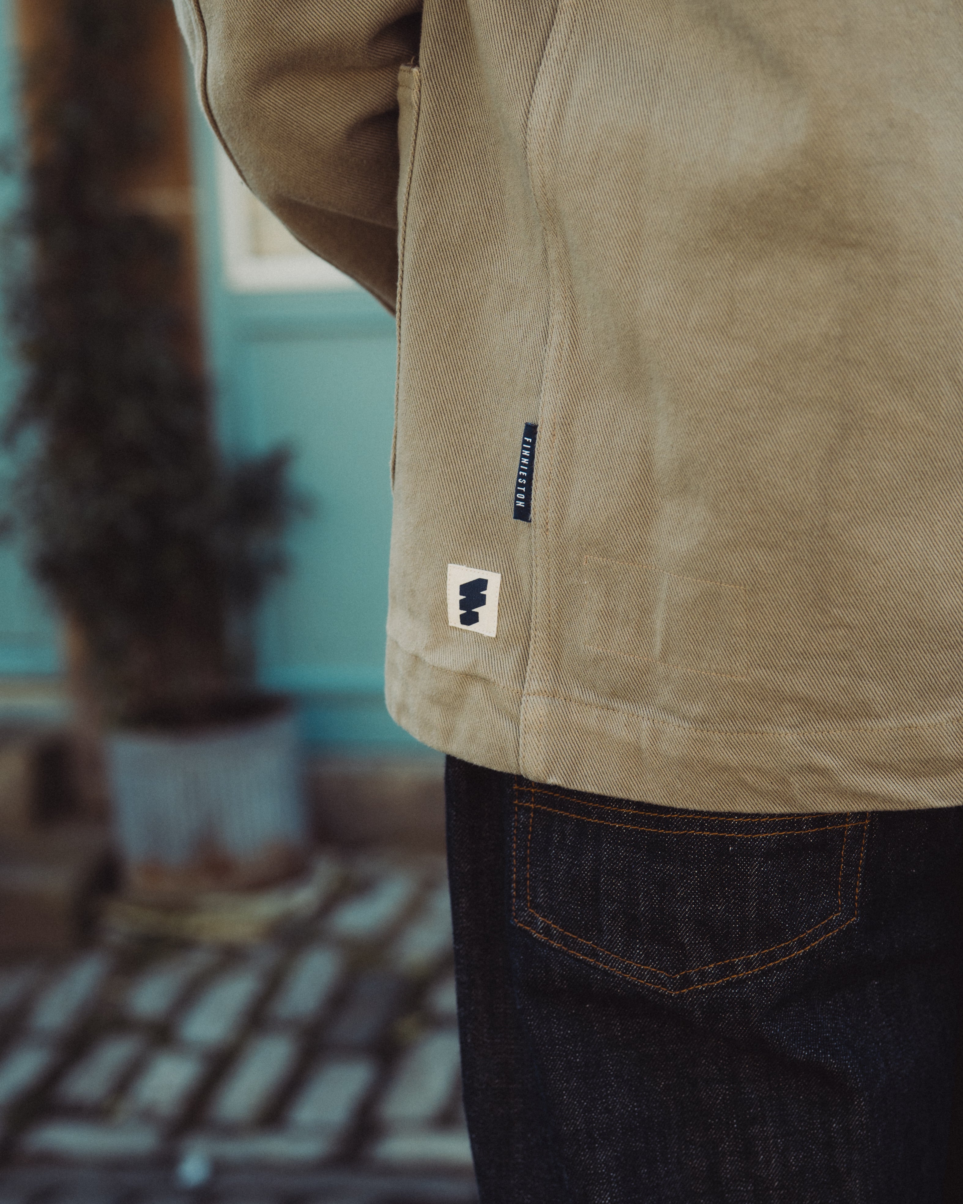 Close-up of a person wearing a beige jacket with a brand logo, blurred indoor background