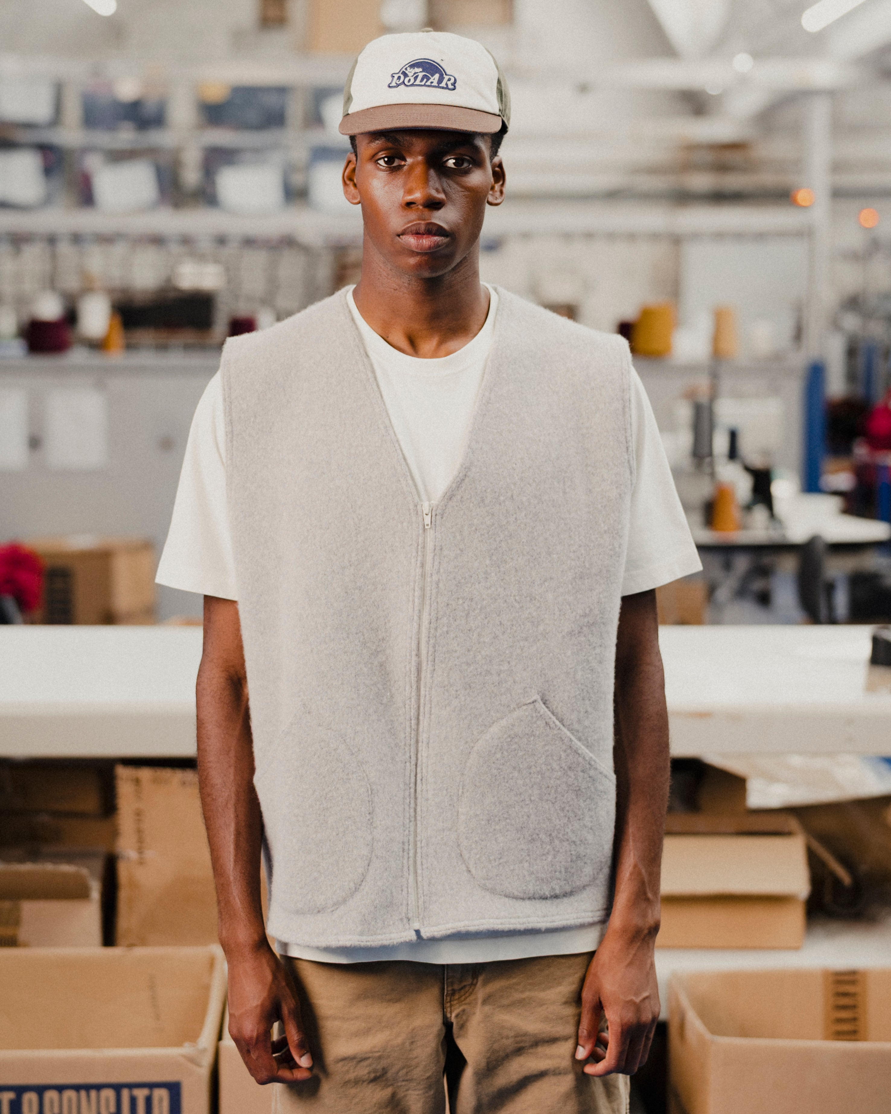 Man wearing a gray wool vest over a white t-shirt with a cap in an indoor setting