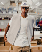 Man wearing a light gray wool vest over a white t-shirt with a cap in an indoor setting