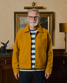 Man wearing a mustard yellow jacket in a room with a painting and lamp in the background