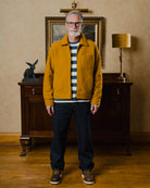 Man wearing a mustard jacket in an interior setting with a lamp and framed picture.