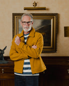 Man in a mustard jacket standing in a room with a painting on the wall