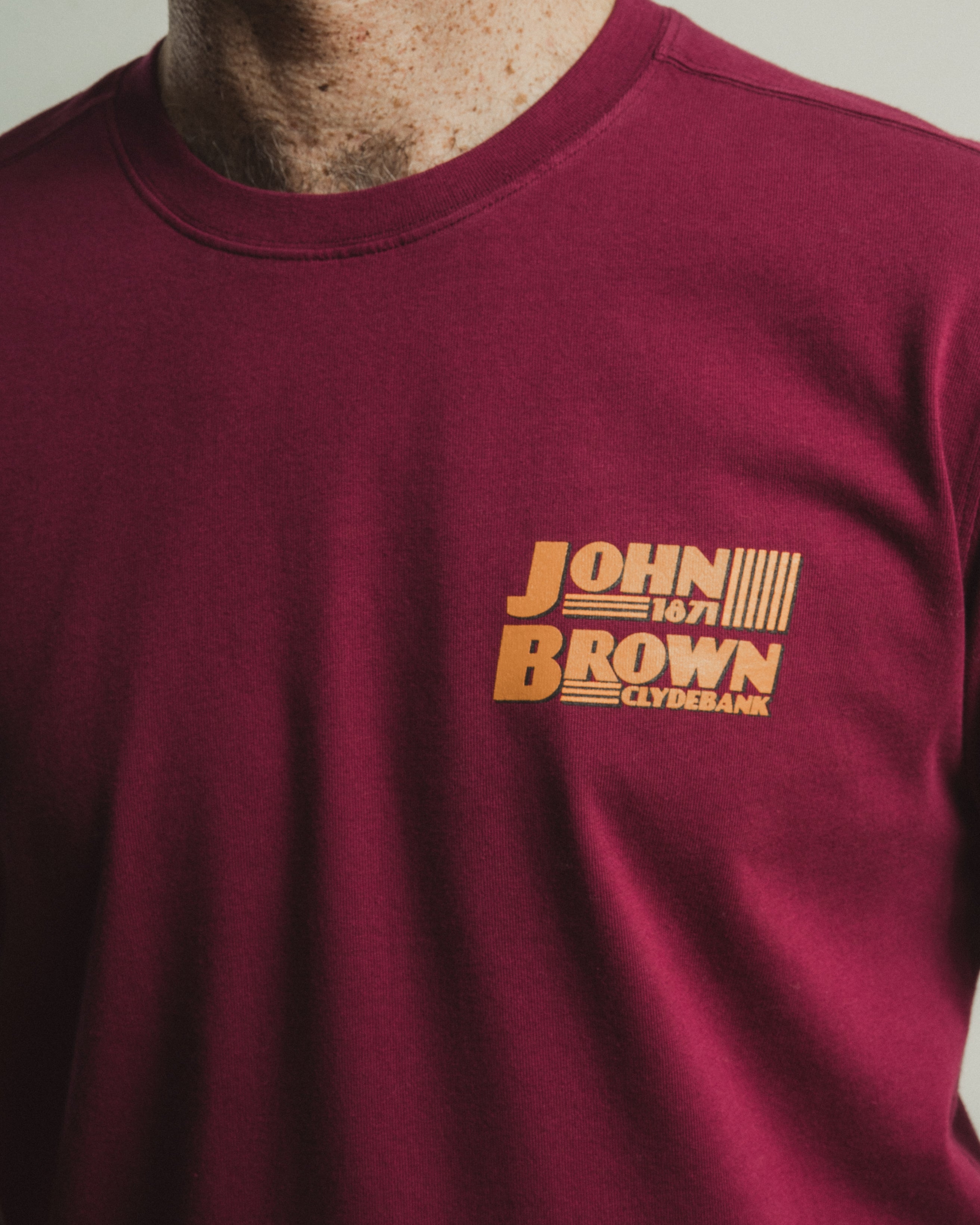 Maroon t-shirt with yellow text on a plain background