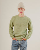 Person wearing a green wool knit sweater and beige beanie against a plain background