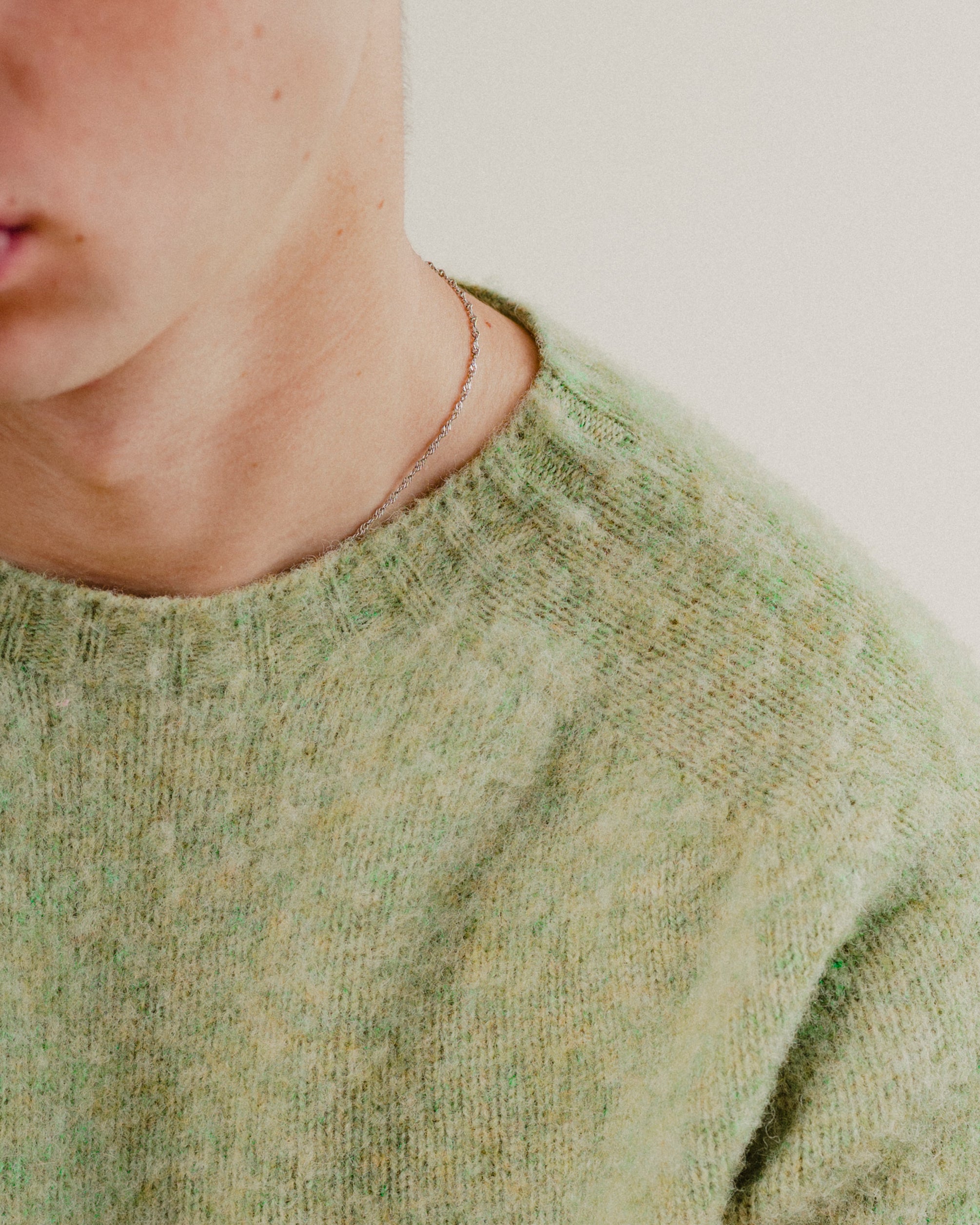 Close-up of a person wearing a green wool knitted sweater with a blurred background