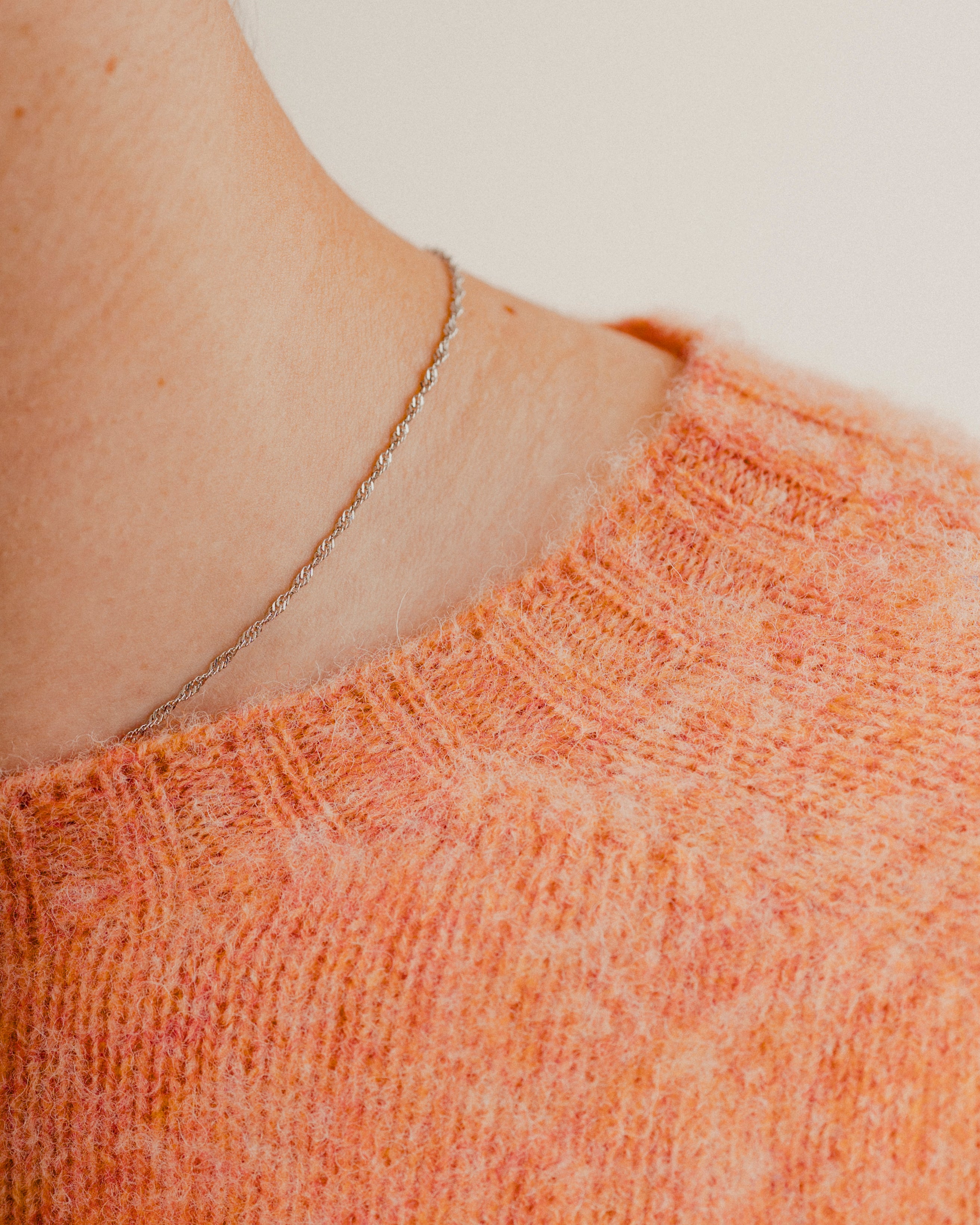 Close up of the neckline of an orange wool knit crewneck made in scotland