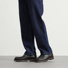 Person wearing dark blue jeans and brown Kleman shoes on a light gray background