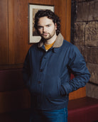 Man wearing a blue jacket in a room with wooden paneling and a stone wall.