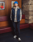 Man wearing a blue beanie and vest standing in a room with wooden walls and red benches.