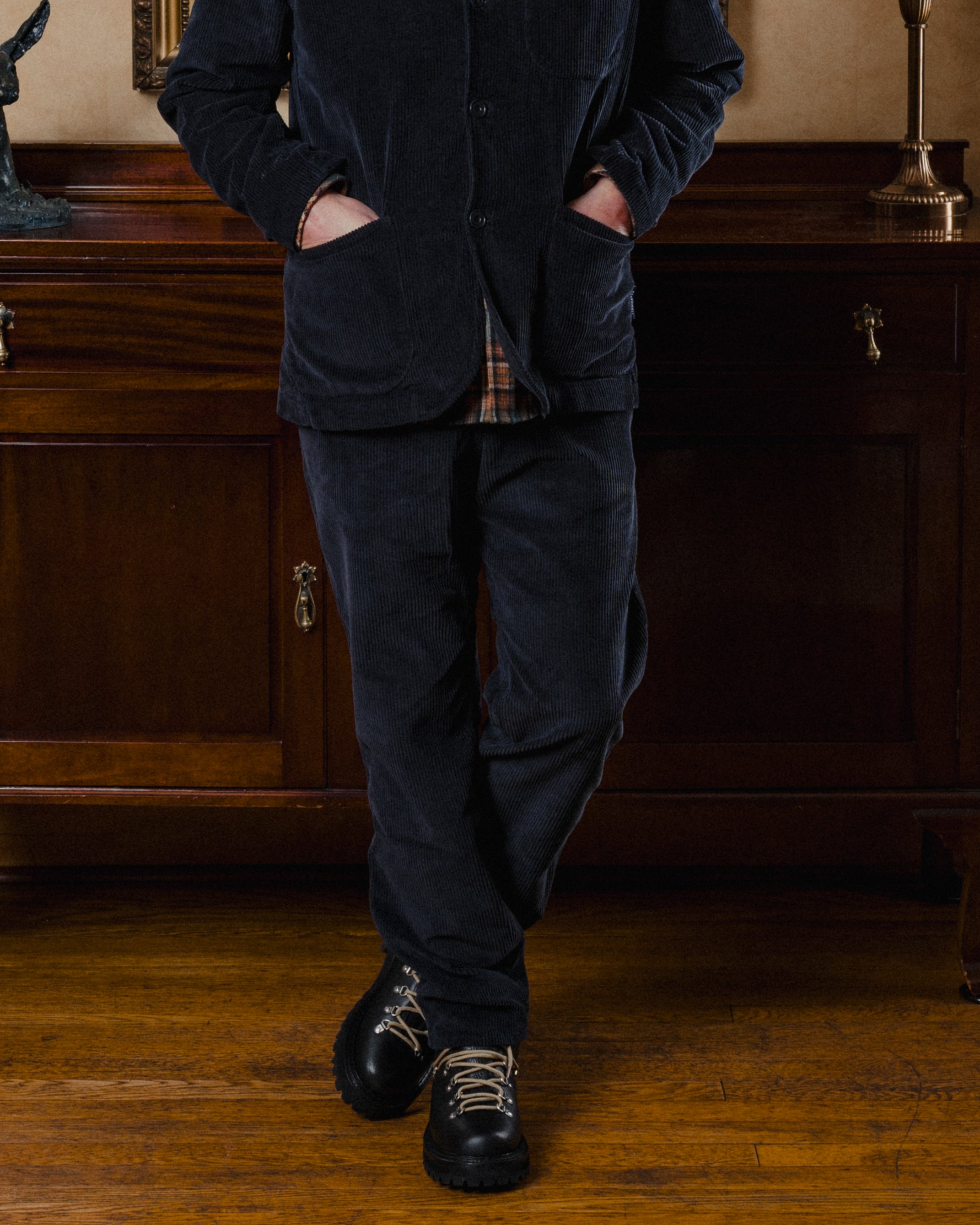 Person wearing a dark blue corduroy suit standing in a room with wooden furniture.