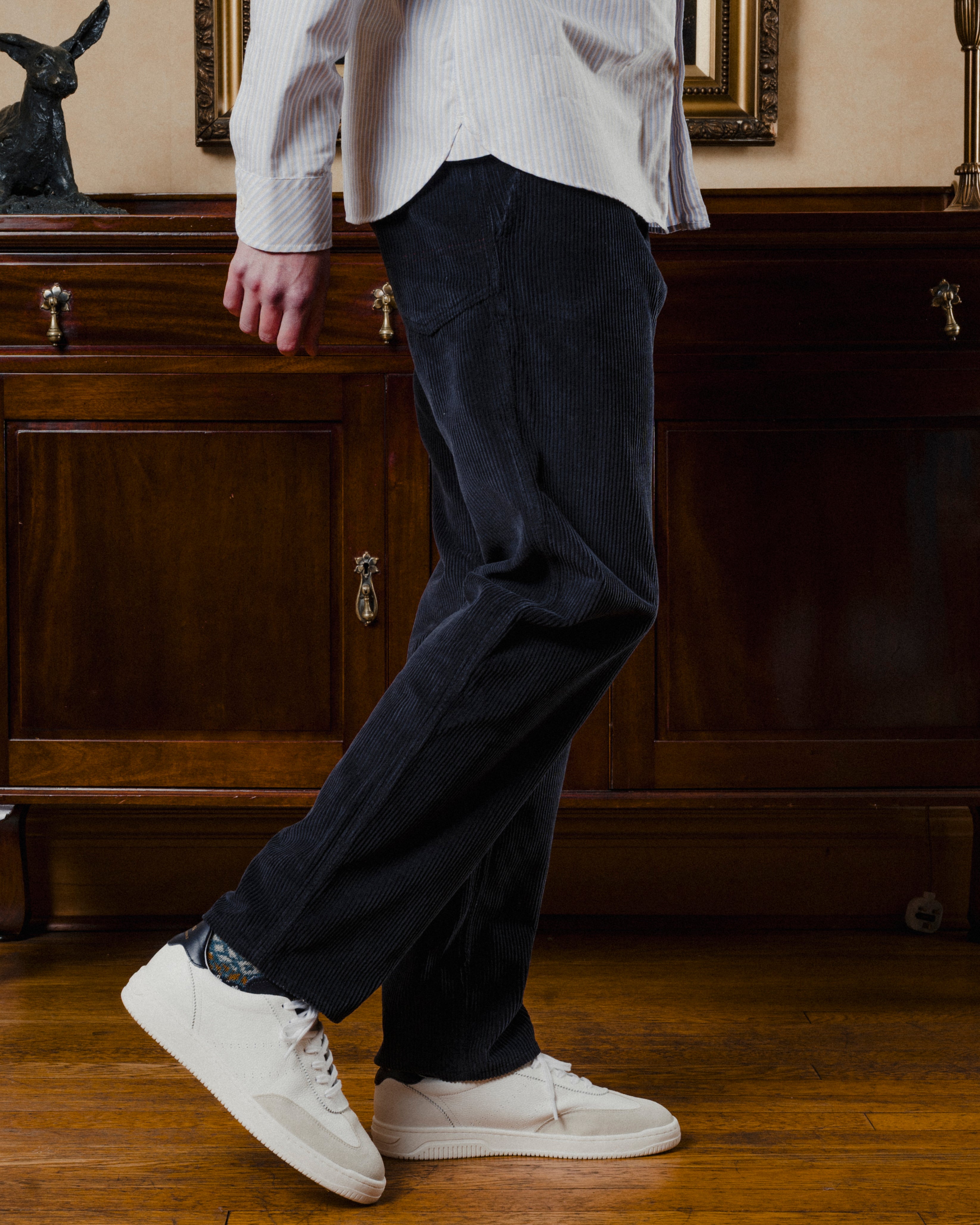 Person wearing dark pants and white sneakers in a room with wooden furniture.