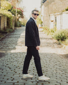 Man in a suit walking on a cobblestone street with greenery and a building in the background