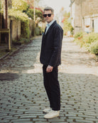 Man in a dark suit and sunglasses standing on a cobblestone street.