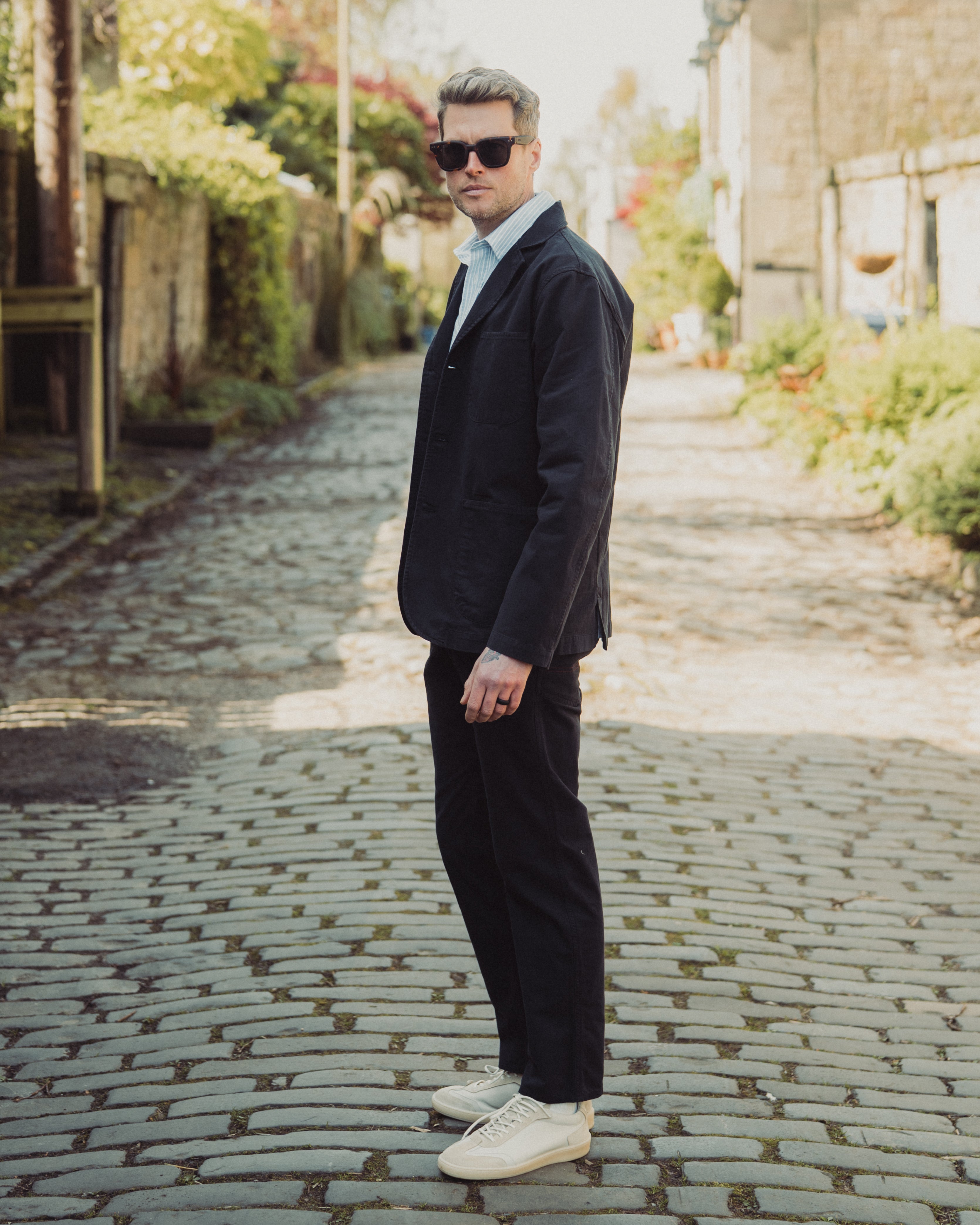 Man in a dark suit and sunglasses standing on a cobblestone street.