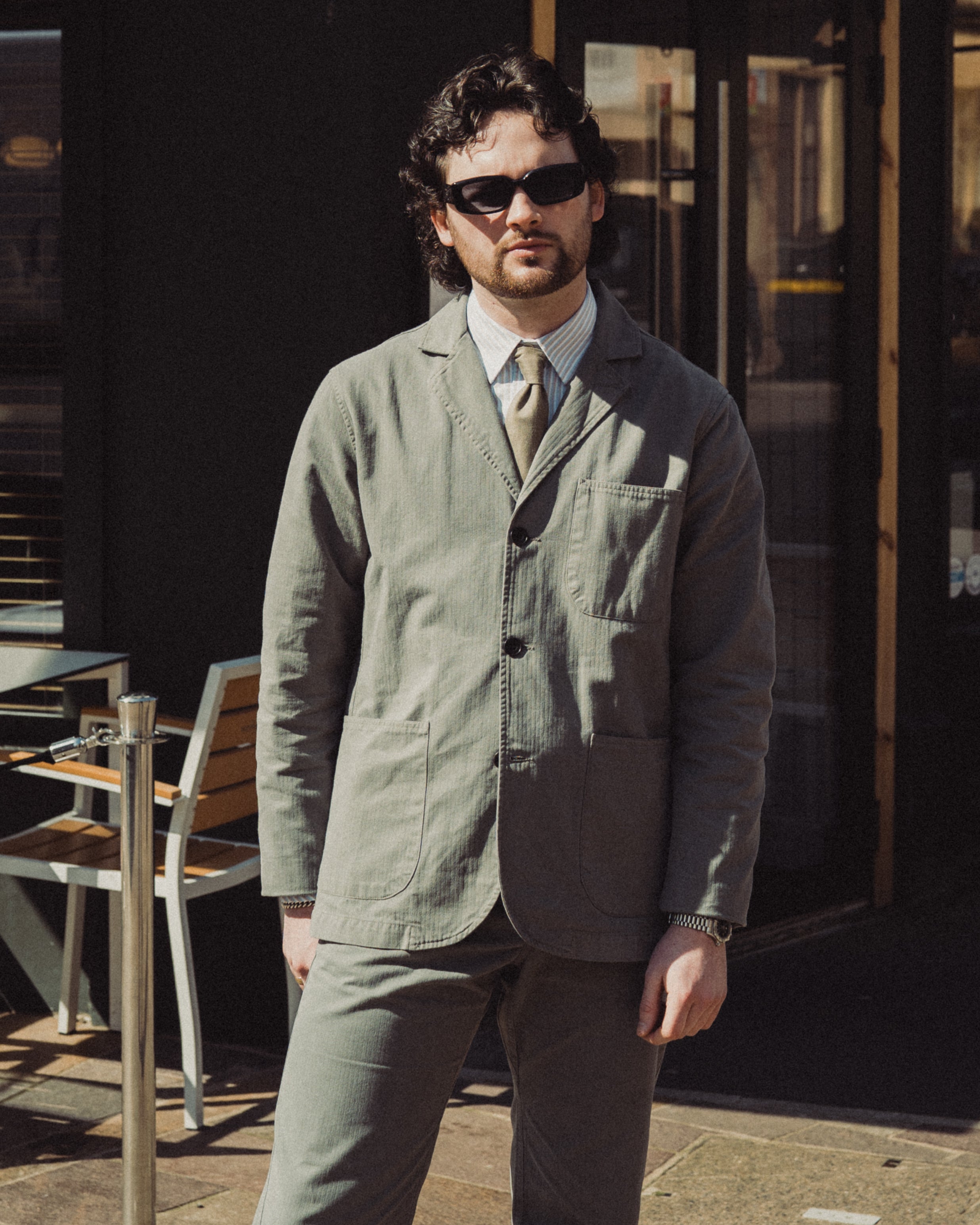 Man wearing a green jacket and brown pants standing outdoors.