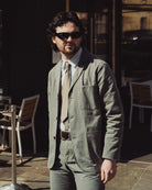 Man wearing sunglasses and a green jacket standing outdoors.