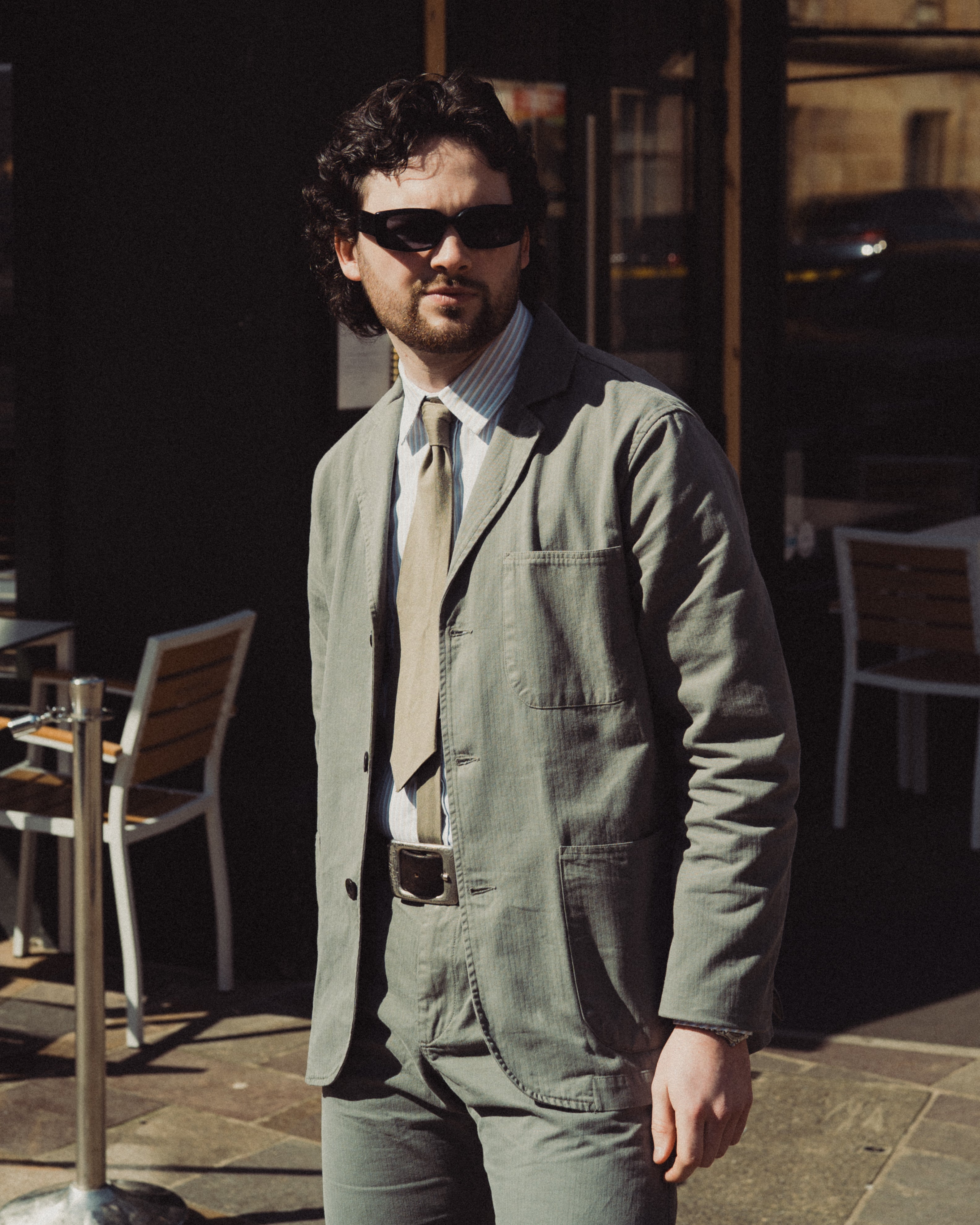 Man wearing sunglasses and a green jacket standing outdoors.