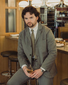 Man in a gray suit sitting at a bar holding a drink