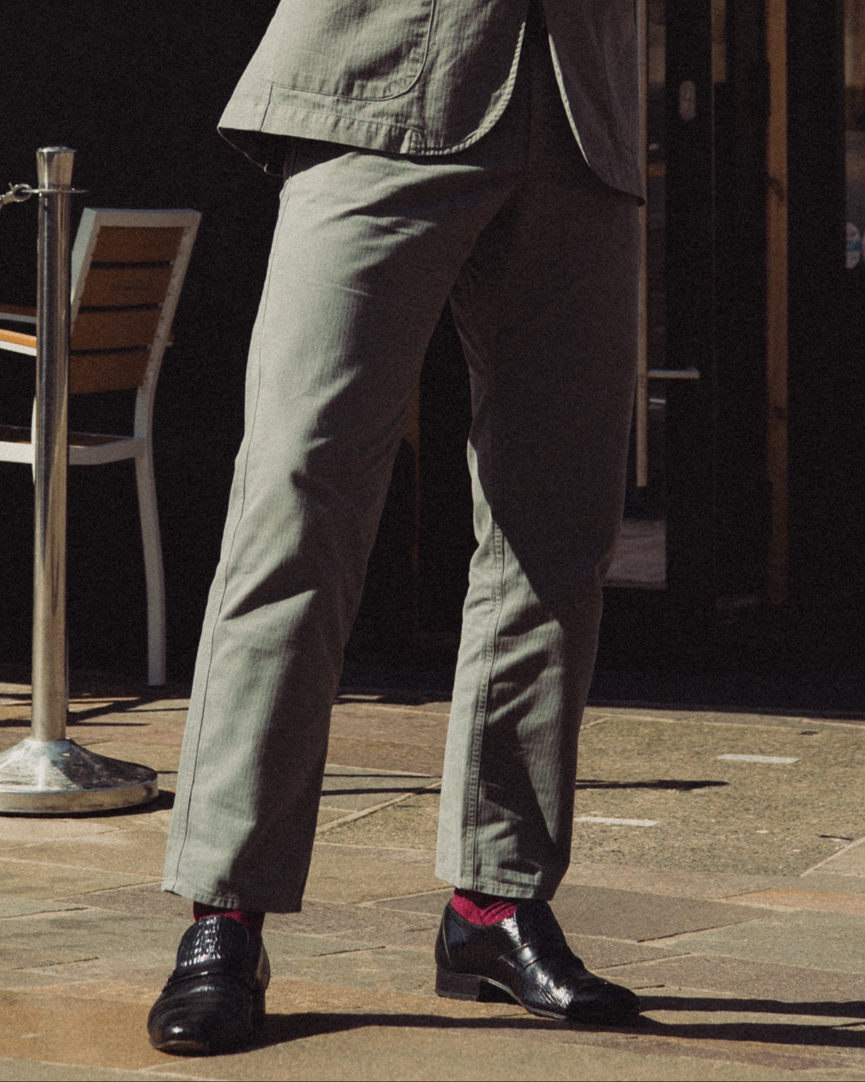 Man in a suit standing outside a corner shop with tables and chairs.