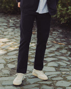 Man in dark coat and sunglasses standing on a stone path with greenery in the background
