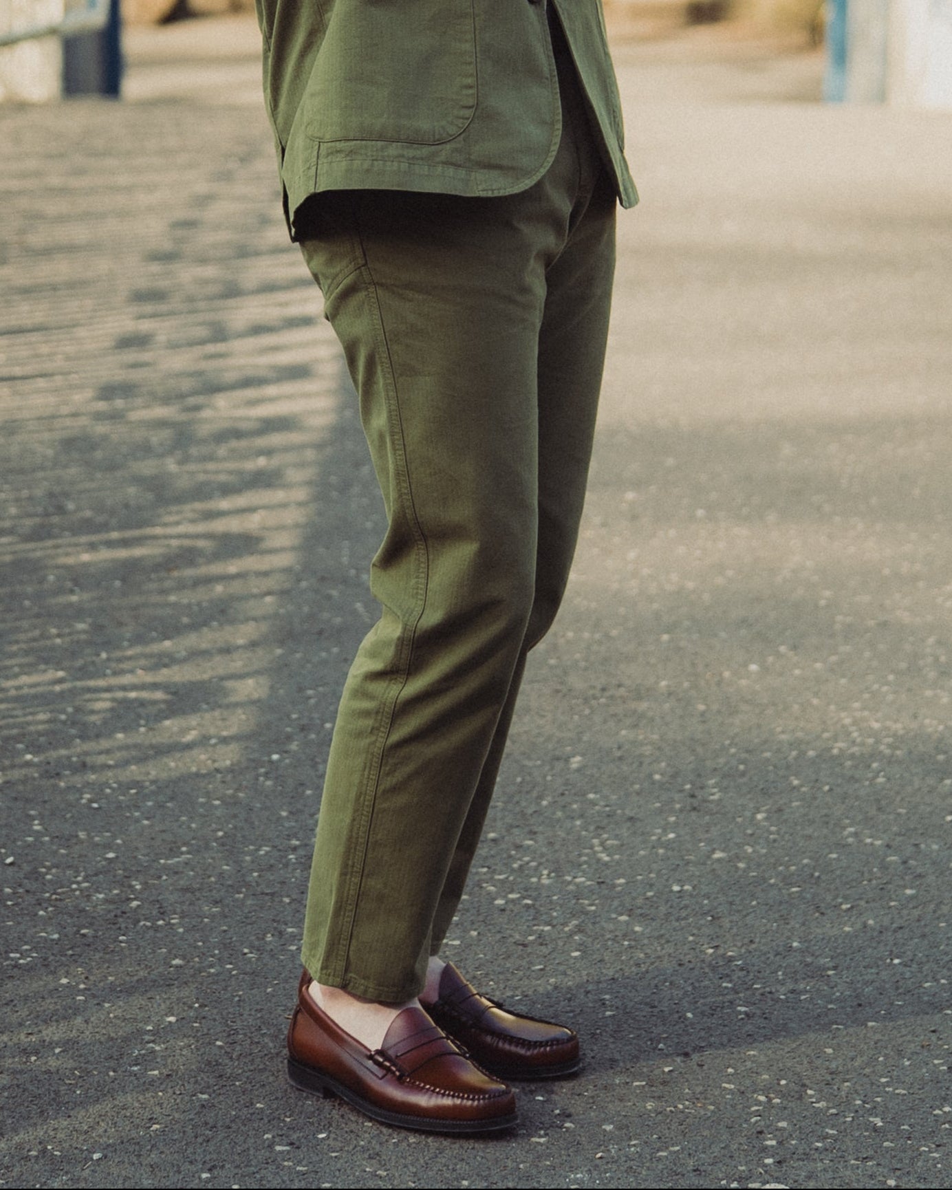 Man in a green suit standing on a pathway with white gates and greenery in the background
