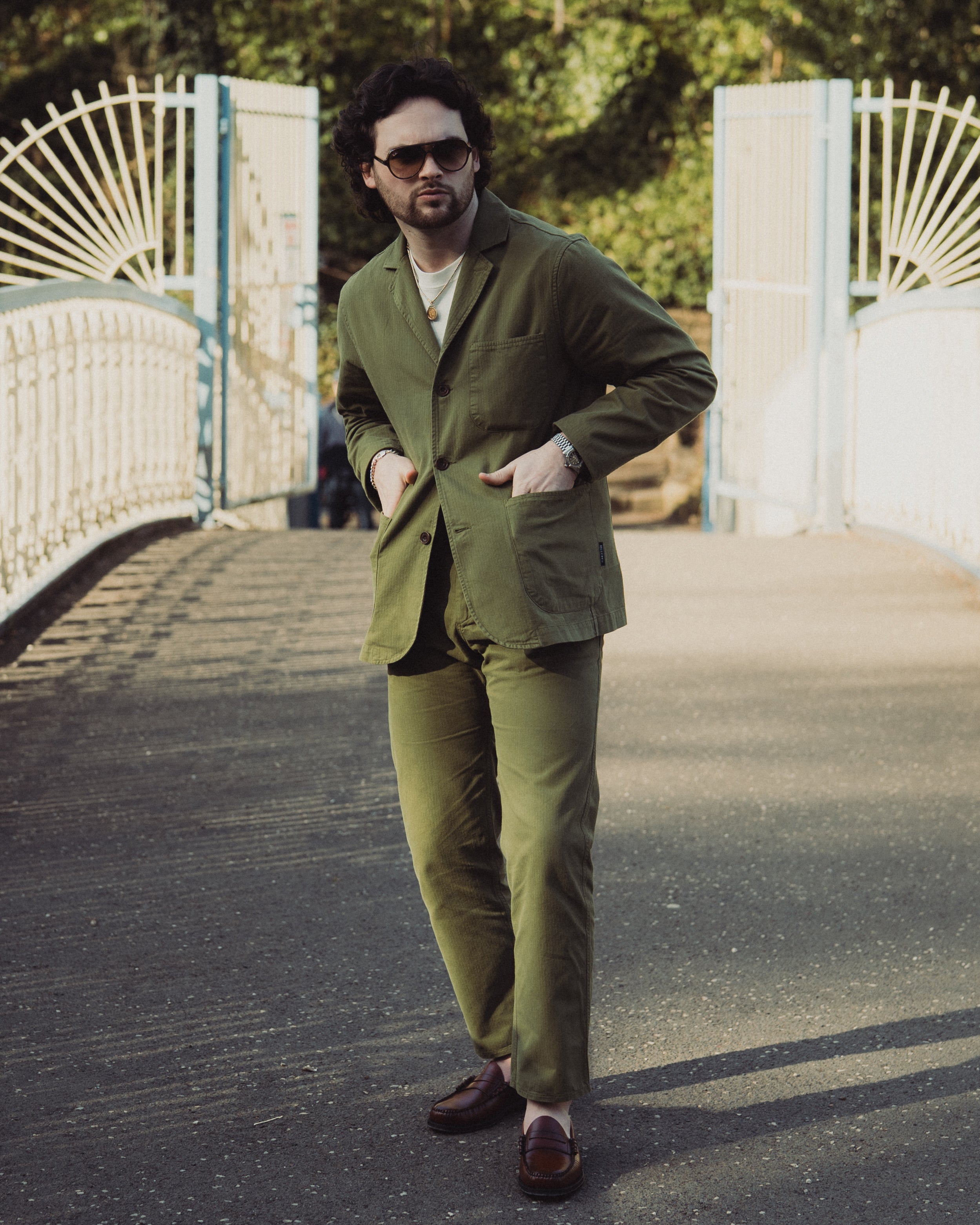 Man in a green suit standing on a bridge with white railings.