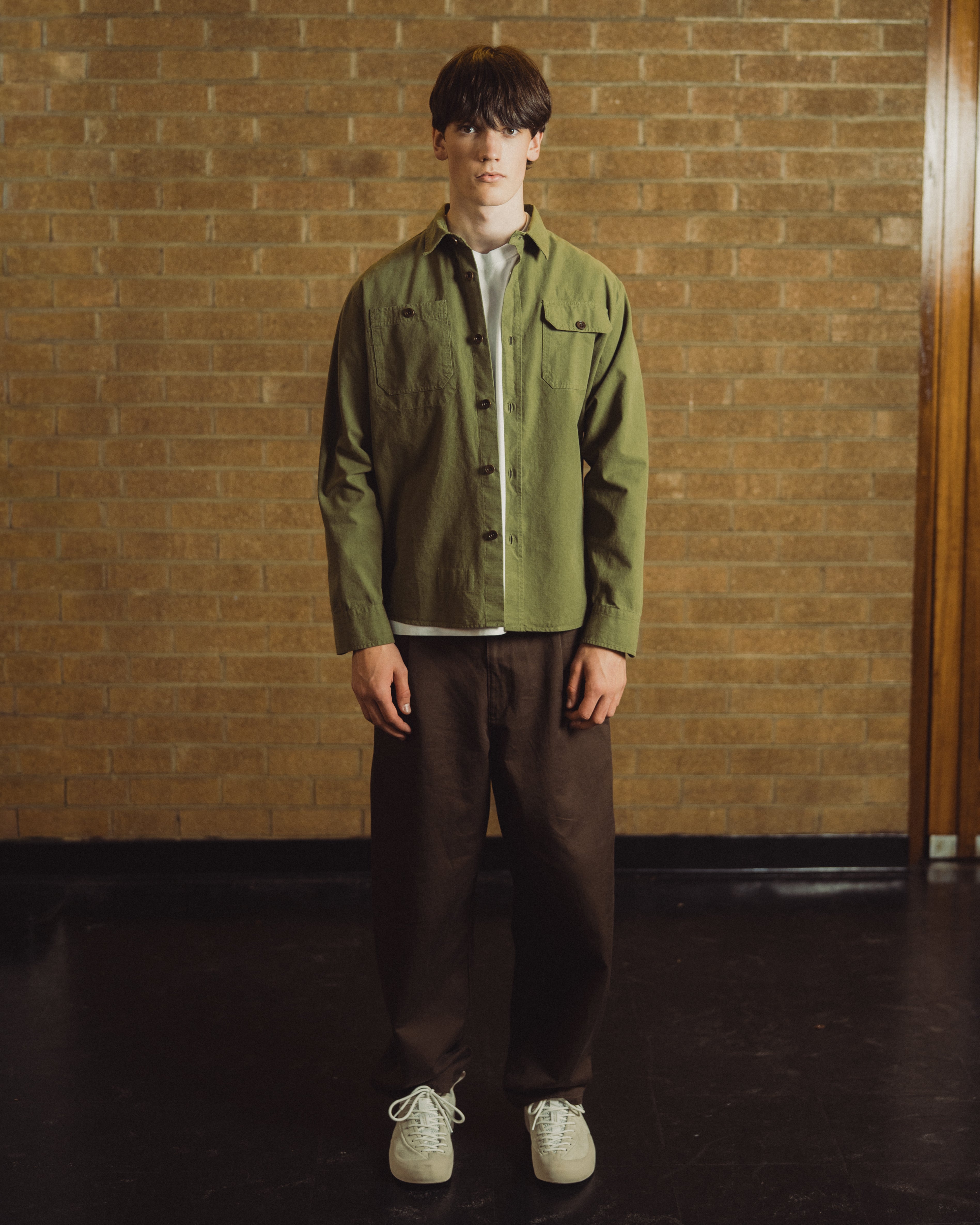 man with green overshirt in front of brick wall