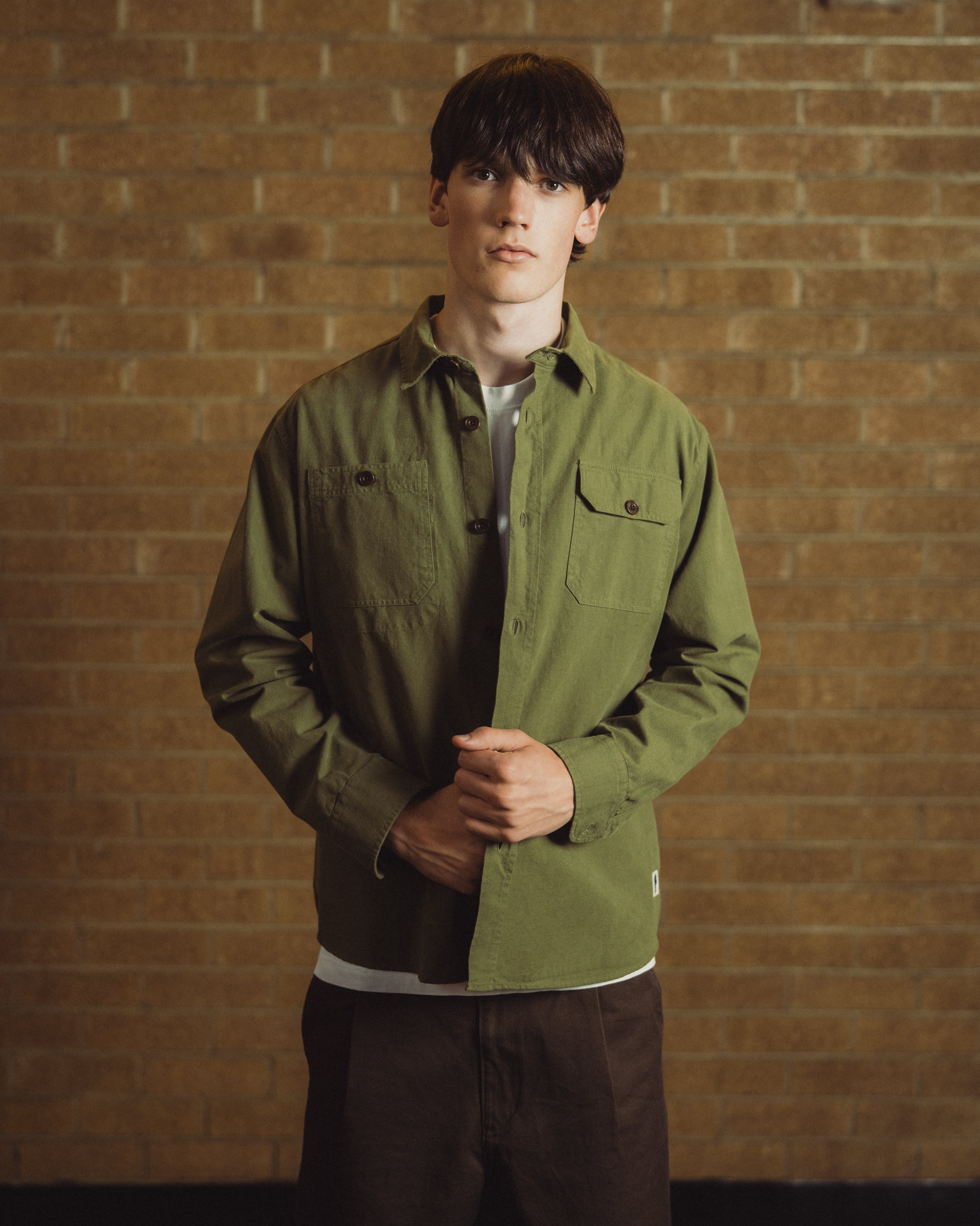 man with green overshirt in front of brick wall