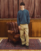 Blue organic cotton sweat , model standing in front of brown leather armchair
