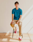 Man sitting on a stool wearing a blue t-shirt, beige pants, and red sneakers in a well-lit room.