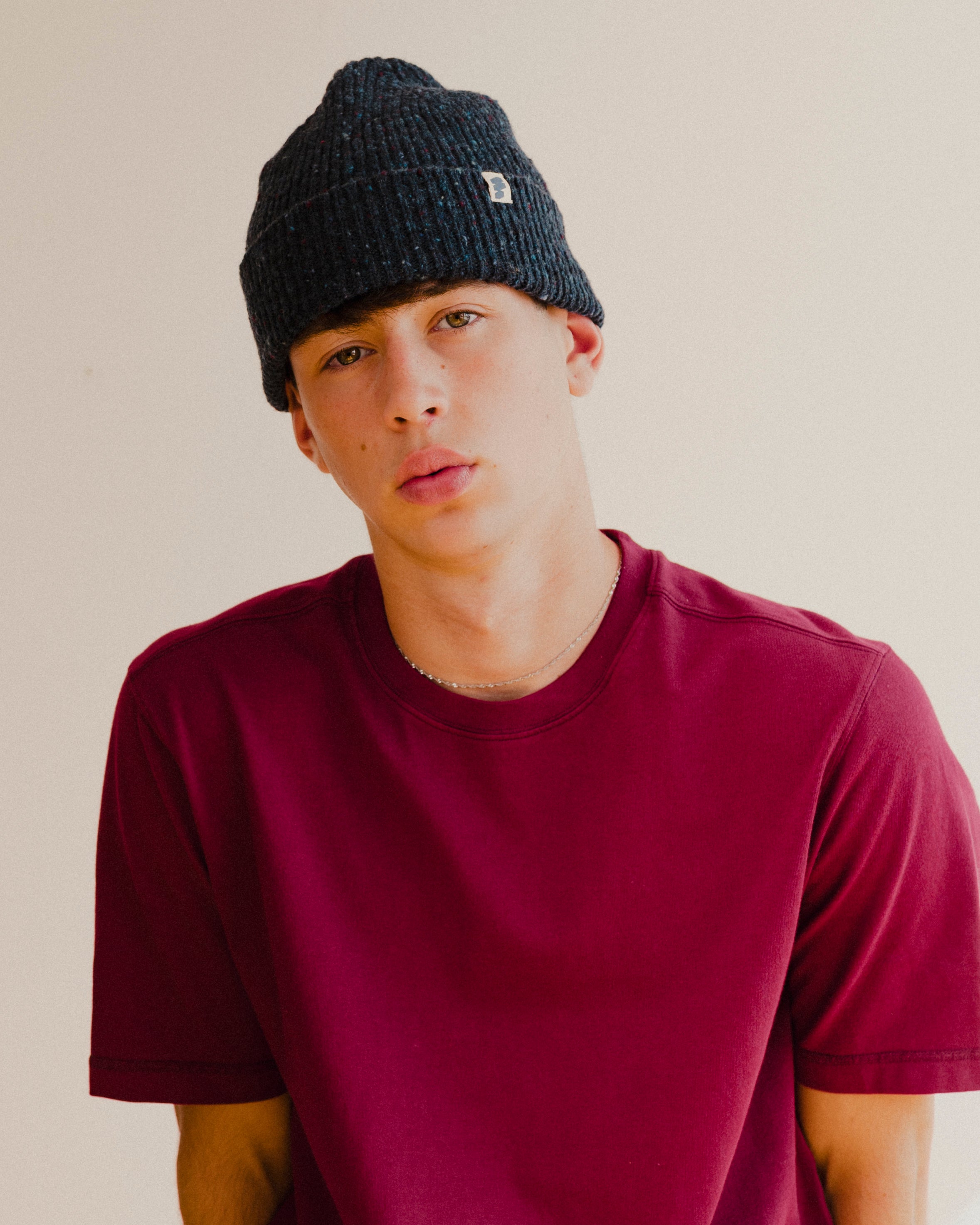 Person wearing a dark navy blue beanie and maroon red shirt against a plain background