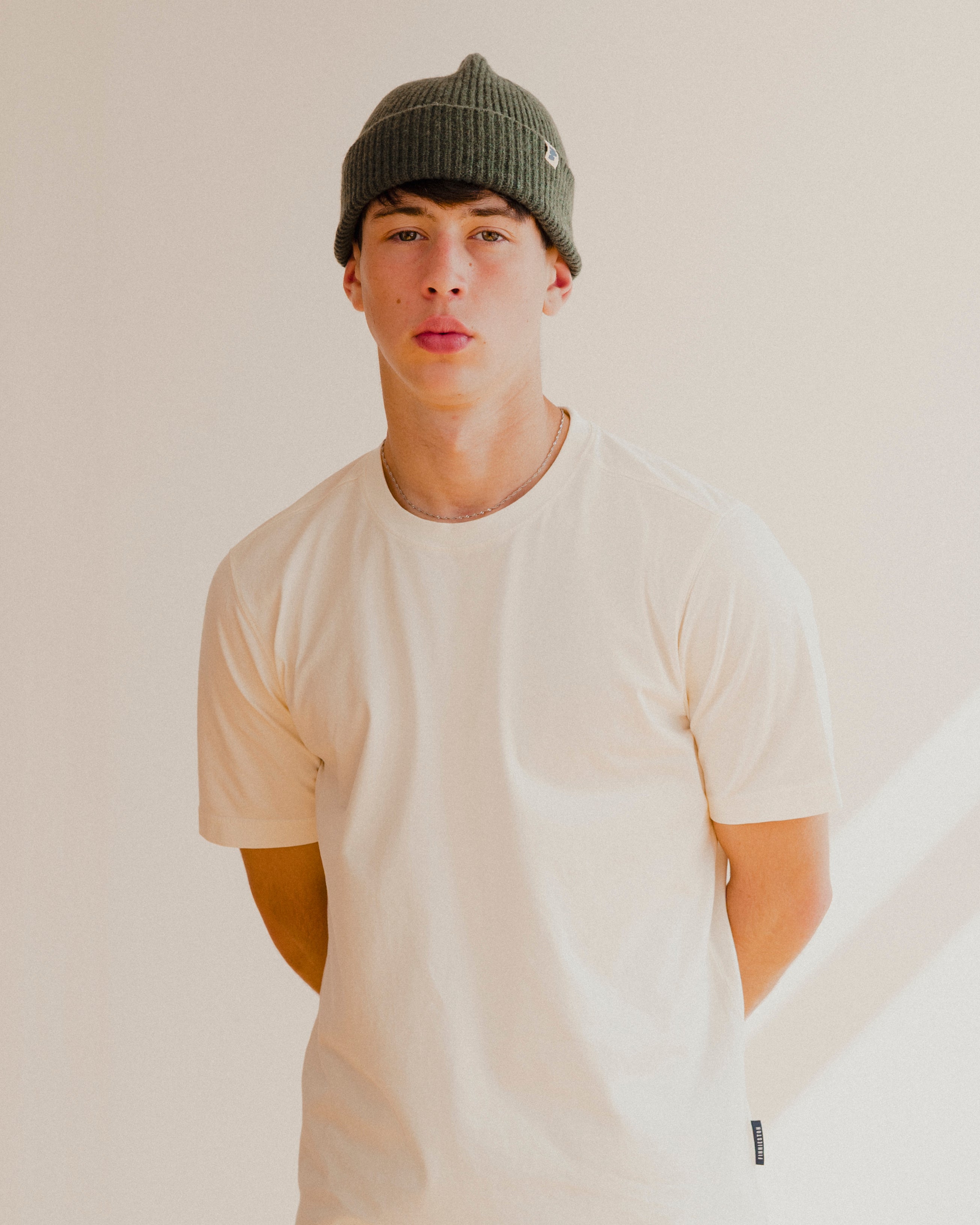 Person wearing a white t-shirt and green beanie against a plain background