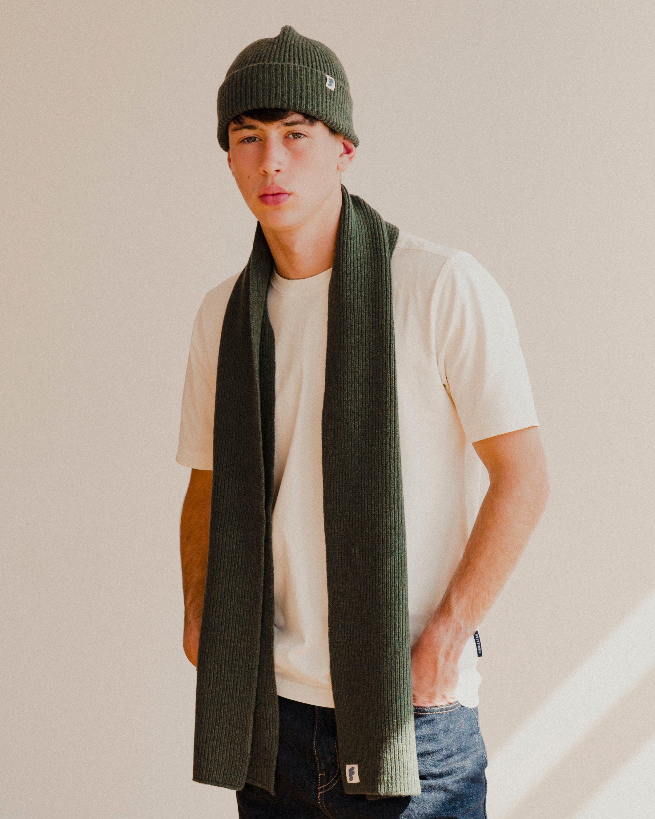 Person wearing a green beanie plain white t-shirt and scarf with a plain background