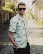 Man wearing a light-colored patterned shirt and sunglasses outdoors.