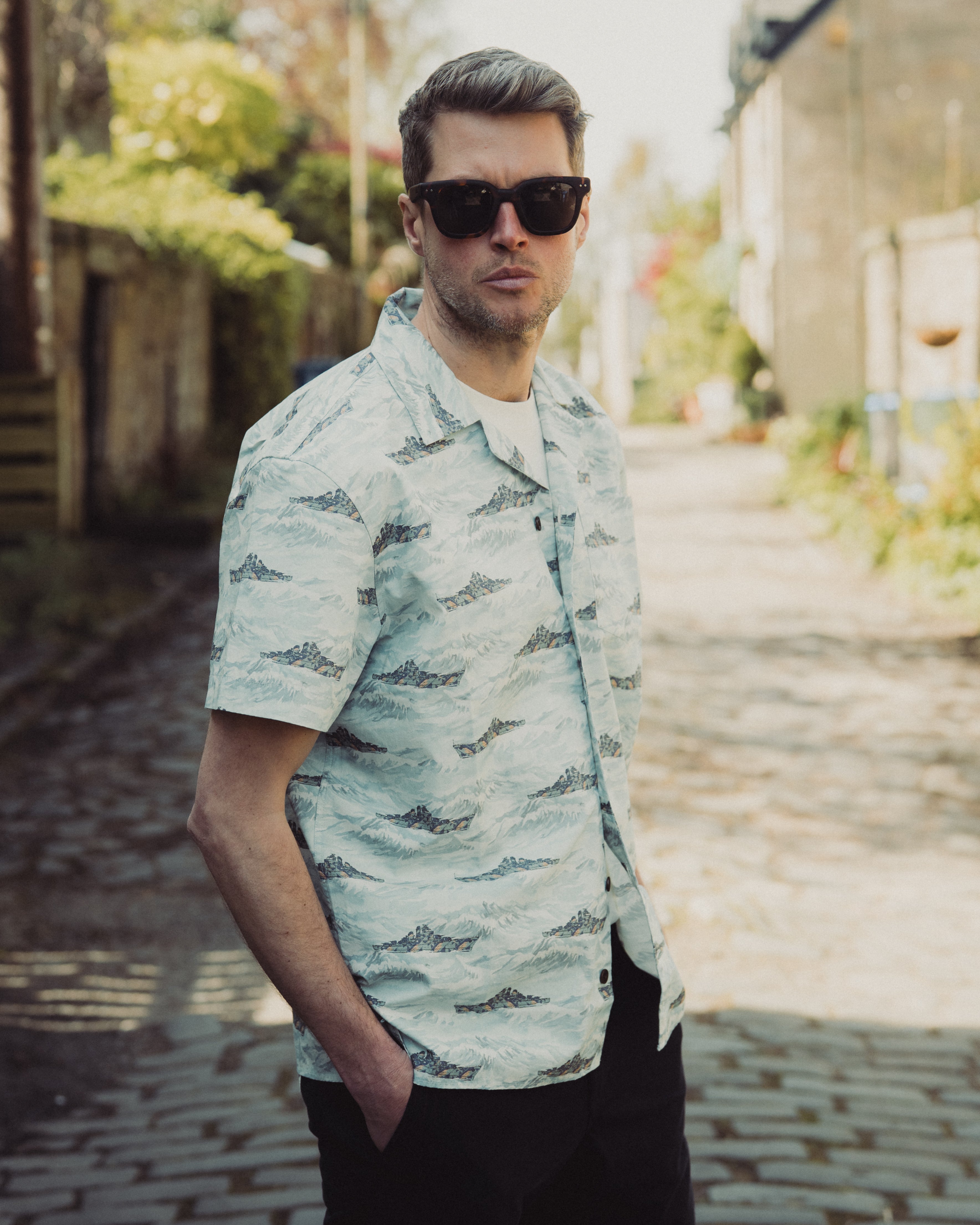 Man wearing a light-colored patterned shirt and sunglasses outdoors.