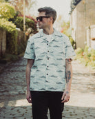 Man wearing a light green patterned shirt standing outdoors on a sunny day.