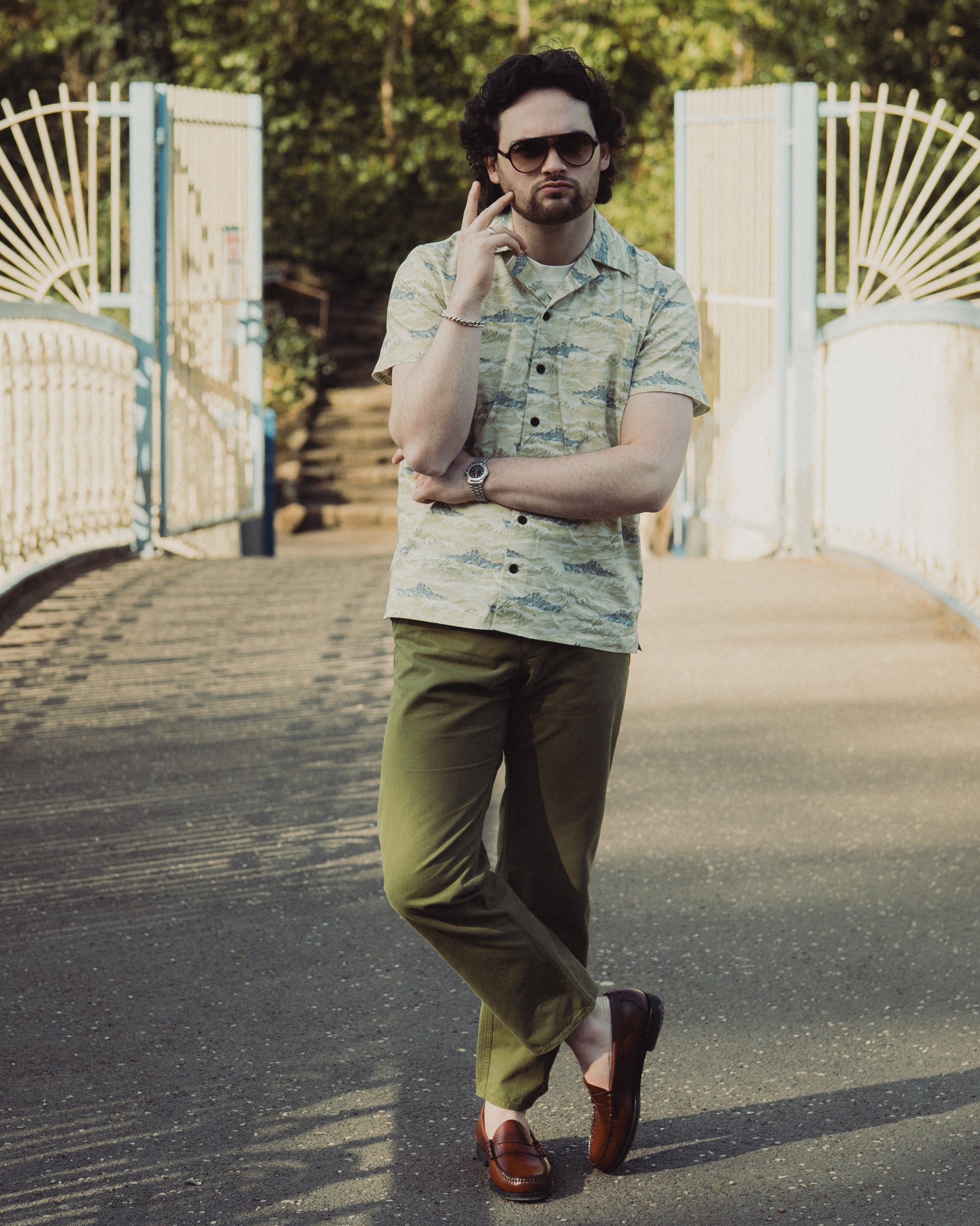 Man in a patterned shirt and green pants standing on a bridge